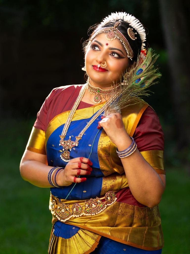 bharatanatyam dancer nandini raju poses in dance costume holding a peacock feather